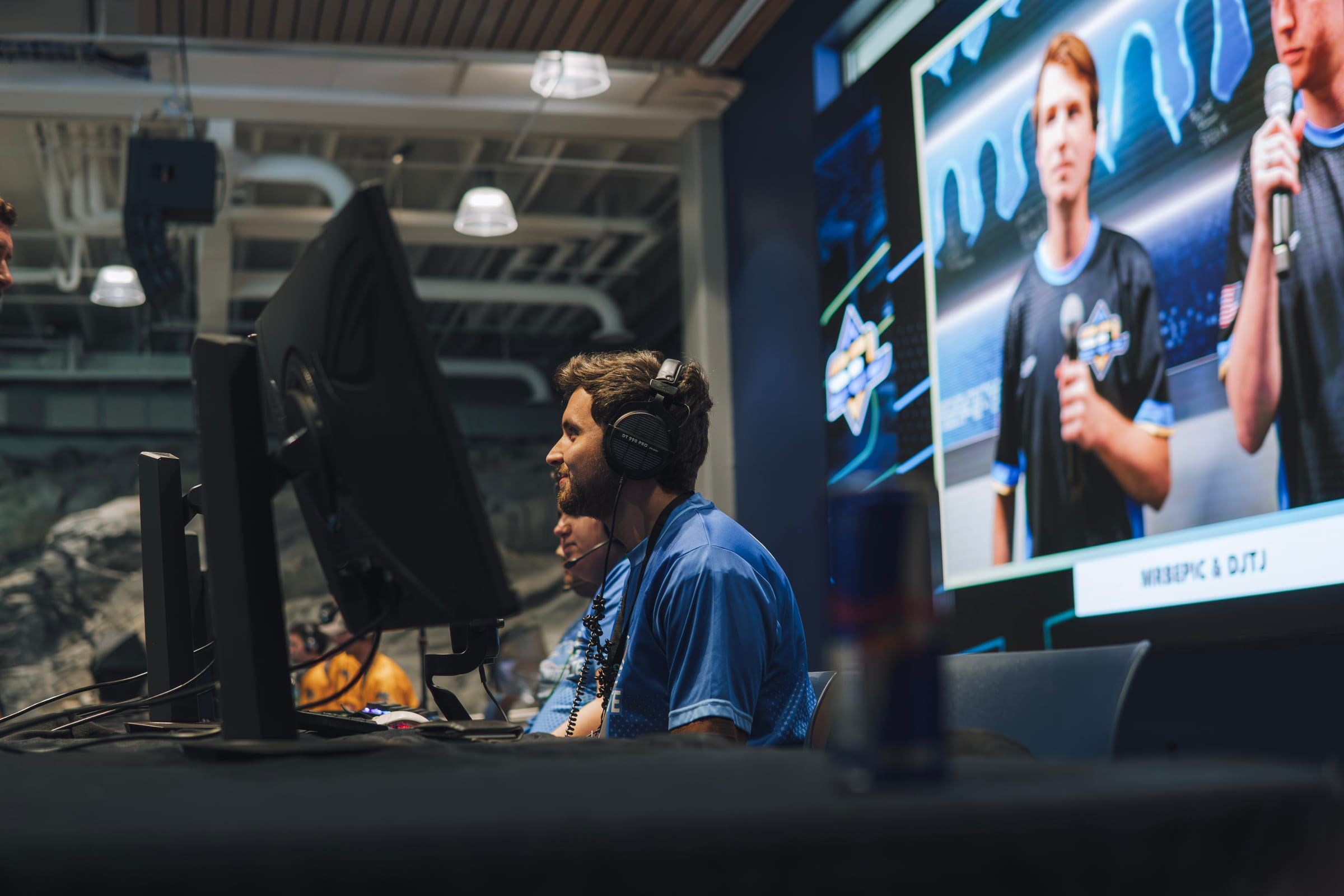 SEL competitor at a gaming station with broadcast screens behind them